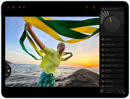 Parte da frente do iPad Air mostrando a edi??o da foto de uma pessoa segurando um tecido verde e amarelo contra o p?r do sol na praia, com as ferramentas de edi??o visíveis no lado direito