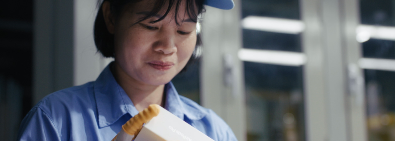 Funcionária com uniforme de trabalho de corpo inteiro e óculos de prote??o observa a montagem do Apple Watch