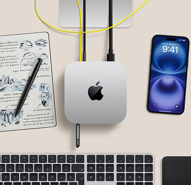 Vue du dessus d’un Mac mini argent sur un bureau avec des cables et un disque flash branchés dans les ports, avec un clavier sans fil, un pavé tactile, un iPhone et un cahier de notes