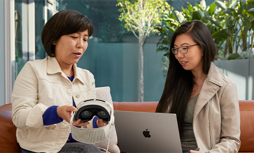 Jessica 在室內(nèi)使用 MacBook，通往露臺(tái)的門開著，她和一位 Apple 同事坐在一起，對(duì)方正在向她展示 Apple Vision Pro。