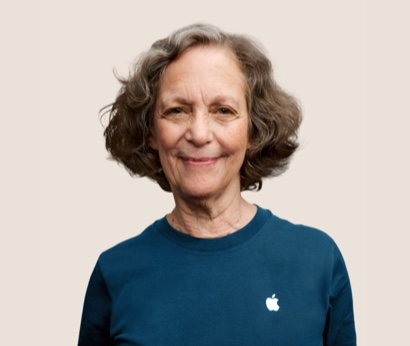 Portr?t eines l?chelnden Apple Retail Teammitglieds mit gewellten dunkelgrauen Haaren.