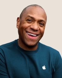 Portr?t eines l?chelnden Apple Retail Teammitglieds mit kurzen dunkelgrauen Haaren.