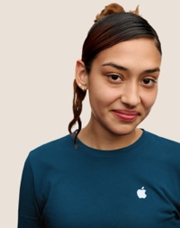 Portr?t eines l?chelnden Apple Retail Teammitglieds mit langen dunklen Haaren und pinken Str?hnen.