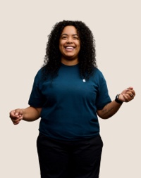 Portr?t eines l?chelnden Apple Retail Teammitglieds mit langen dunklen Locken.