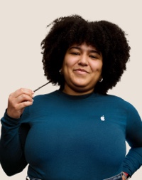 Portr?t eines l?chelnden Apple Retail Teammitglieds mit langen dunklen Locken.