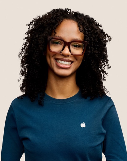 Portr?t eines l?chelnden Apple Retail Teammitglieds mit langen dunklen Locken und Brille.