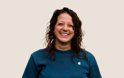 Portr?t eines l?chelnden Apple Retail Teammitglieds mit langen, gewellten dunklen Haaren.