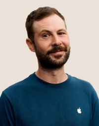 Portr?t eines l?chelnden Apple Retail Teammitglieds mit dunklen Haaren und Bart.