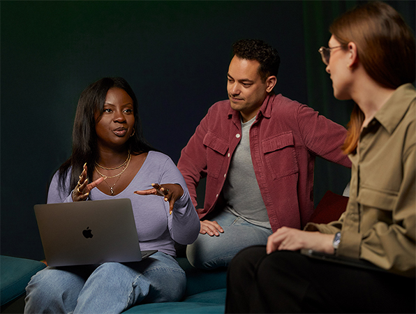 Drie teamleden van Apple Software & Services zitten op een bank en zijn met elkaar in gesprek. Een van hen heeft een MacBook.