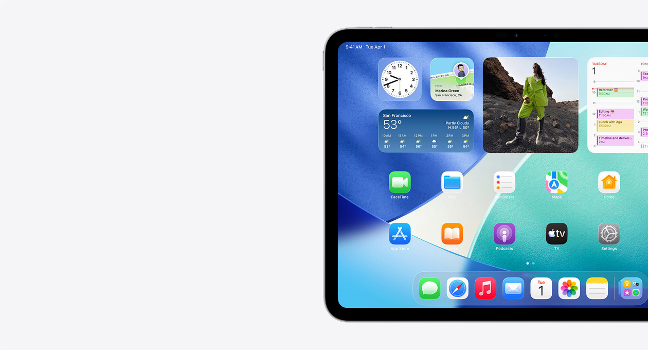 iPad, orientace na ?í?ku, pouze levá strana obrazovky, plocha s widgety v?etně pr?hlednych hodin s efektem Liquid Glass, aplikace Najít, widgetu Po?así, dvou ?ádk? men?ích aplikací a Docku