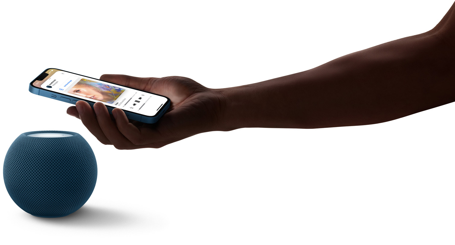 Der HomePod mini in Blau und eine Hand, die ein iPhone über den HomePod mini h?lt. Auf dem iPhone Display wird Musik abgespielt.