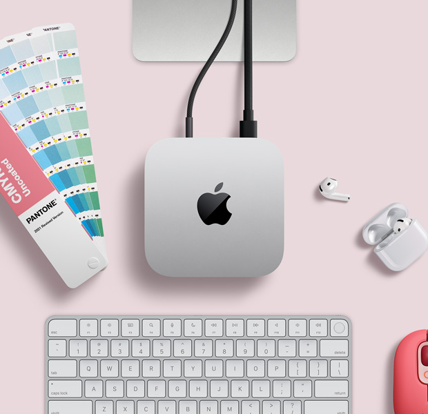 俯視圖展示銀色 Mac mini 擺放在桌上，旁邊放有 AirPods、一個粉紅色無線鍵盤、粉紅色無線滑鼠，以及一疊扇狀顏色卡。