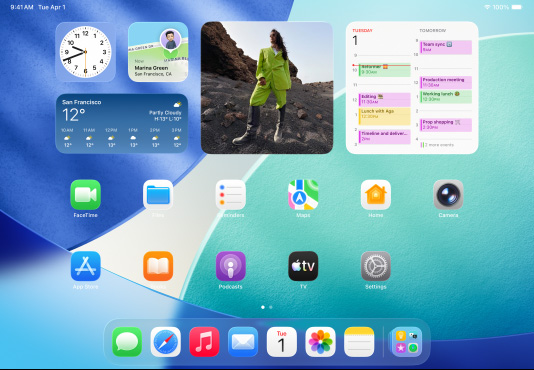 三款型號的 iPad 橫向放置，放在中間的一部位於另外兩部 iPad 的前方。Apple Pencil 以磁力貼合在中間那部 iPad 的頂部，其主畫面展示 Liquid Glass 效果的彩色 app 圖像。位於左邊的 iPad 螢?zāi)徽故绢A(yù)覽程式 app，而右邊的螢?zāi)粍t展示主畫面，多個檔案從 Dock 上以扇形垂直展開