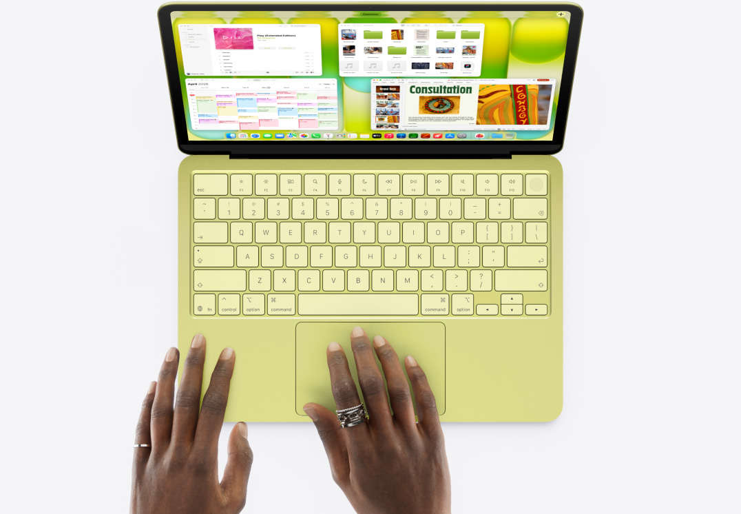 Prikaz MacBooka Neo u citrusnoj boji, na ?ijem trackpadu osoba dr?i ruku, a na zaslonu je otvoreno nekoliko prozora s aplikacijama Glazba, Kalendar i Microsoft Power Point