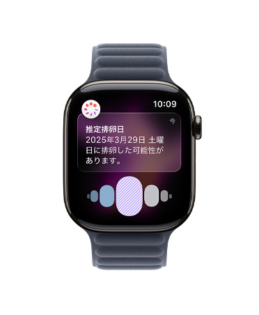 スレートチタニウムケースのApple Watch Series 11。ヘルスケアアプリの周期記録から推定される排卵日の通知が表示されている。Digital Crownが見えていて、ネイビーのマグネティックリンクバンドが取りつけられている