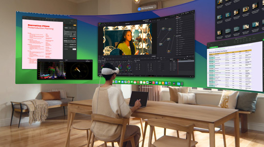 Apple Vision Proを裝著した人が13インチMacBook Proを開いてデスクに座っている。畫面の內(nèi)容が表示されたカーブしたウルトラワイドディスプレイが部屋に投影されている