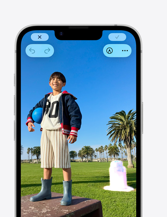 公園のボックスの上に立って微笑む人物の寫真が表示されたiPhoneの畫面。クリーンアップツールを使って背景にあるゴミ箱を削除する方法を示している