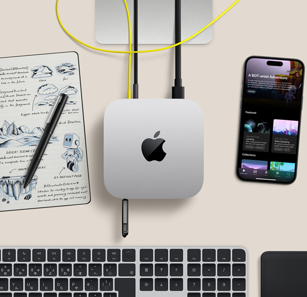 デスク上に置かれたシルバーのMac miniを上から見(jiàn)た図。コードとフラッシュドライブがポートにつながれている。ワイヤレスキーボード、トラックパッド、iPhone、ノートが一緒に配置されている