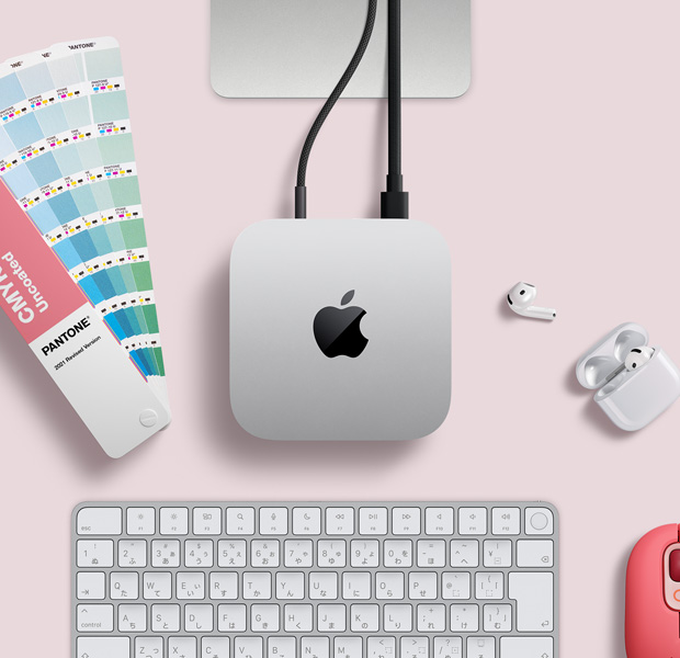 デスク上に置かれたシルバーのMac miniを上から見(jiàn)た図。AirPods、ピンクのワイヤレスキーボード、ピンクのワイヤレスマウス、短冊(cè)型の色見(jiàn)本が一緒に配置されている