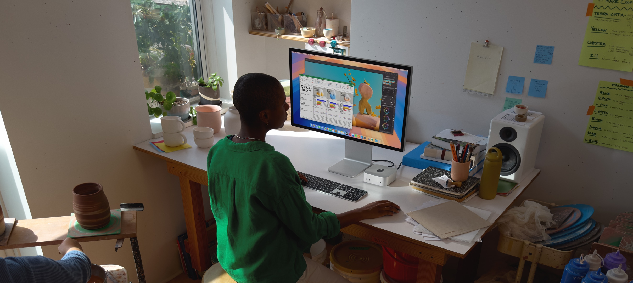 Asmuo naudojasi ?Mac mini“ prie darbo stalo, jis ?iūri ? ekran?, kuriame matomos veikian?ios spalvingos programos