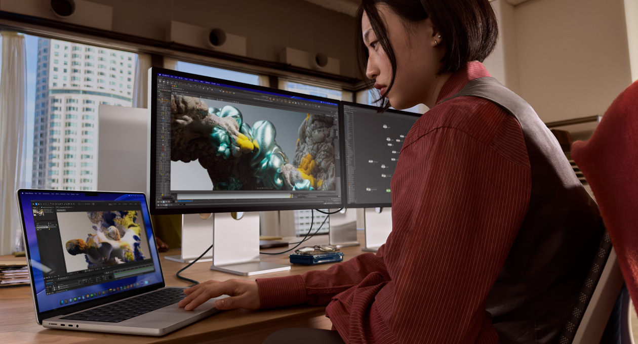 Asmuo, s?dintis ofis? primenan?ioje aplinkoje, dirba su ?MacBook“ ne?iojamuoju kompiuteriu, kuris yra prijungtas prie ?Studio Display XDR“ naudojant ?Thunderbolt 5“ prievad?