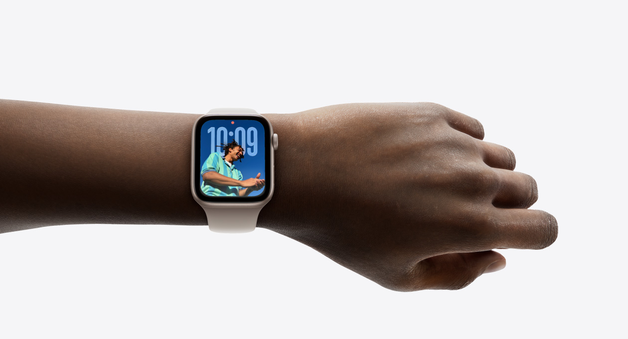 特寫(xiě)畫(huà)面顯示手腕上戴著配上橡膠錶帶的星光色 Apple Watch，展示全新 Liquid Glass 設(shè)計(jì)的時(shí)鐘 app