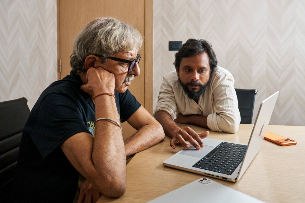 Ritesh Sharma, ?ekim ekibinden bir arkada??yla birlikte masadaki MacBook Pro’ya bakarak ?al???yor. Masada yanlar?nda iPhone 17 Pro Max duruyor.