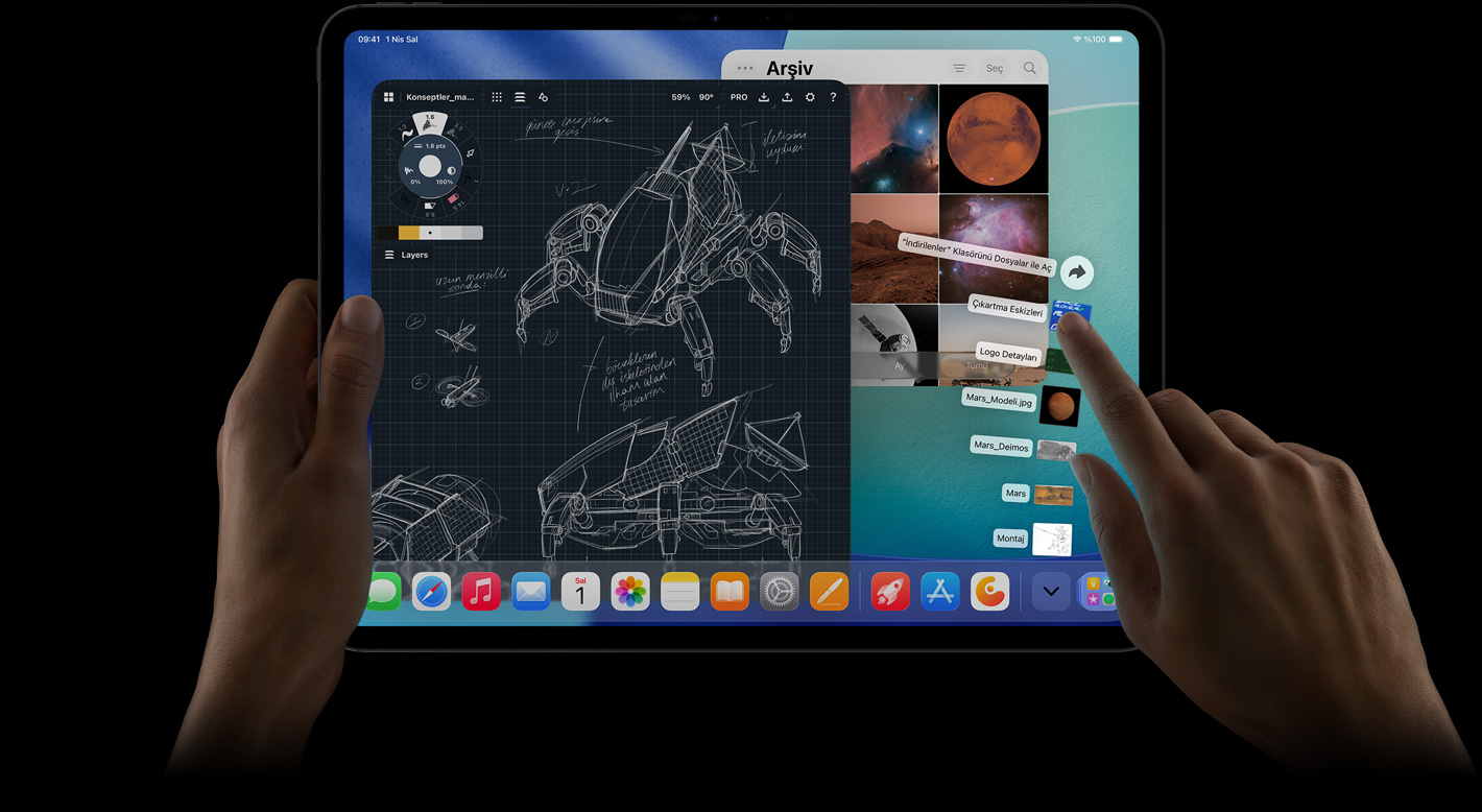iPad Pro, ?nden d?? g?rünüm, yatay pozisyonda, sol el ayg?t? tutuyor, sa? el yelpaze ?eklinde a??lm?? ?ndirilenler klas?rü dosyalar?na i?aret ediyor, ekranda ayr?nt?l? robot projelerinin, el yaz?s? notlar?n ve ?ok say?da tasar?m a?amas?n?n yer ald??? bir foto?raf düzenleme uygulamas? dahil birden fazla uygulaman?n ve Foto?raflar Ar?ivi’nin a??k oldu?u iPadOS 26 arayüzü g?steriliyor