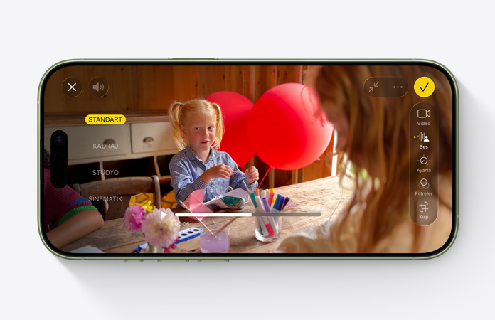 iPhone 17, ?nden d?? g?rünüm, balonlar?n oldu?u bir masada oyun oynayan bir ?ocu?un oldu?u videoda Ses Miksi ?zelli?i kullan?l?yor