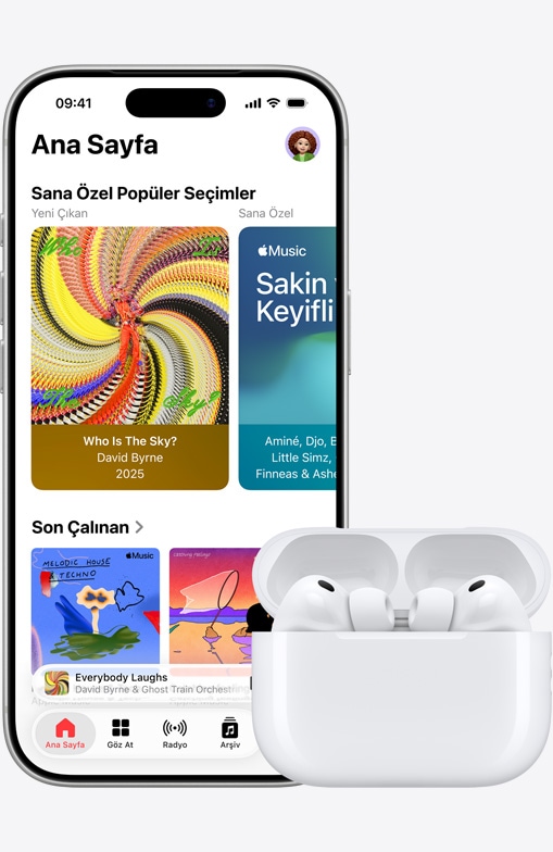 iPhone 17 Pro, ?nden d?? g?rünüm, Ana Ekran’?n a??k oldu?u Apple Music uygulamas?, a??k MagSafe ?arj Kutusu’ndaki AirPods Pro 3’ün yan?nda duruyor