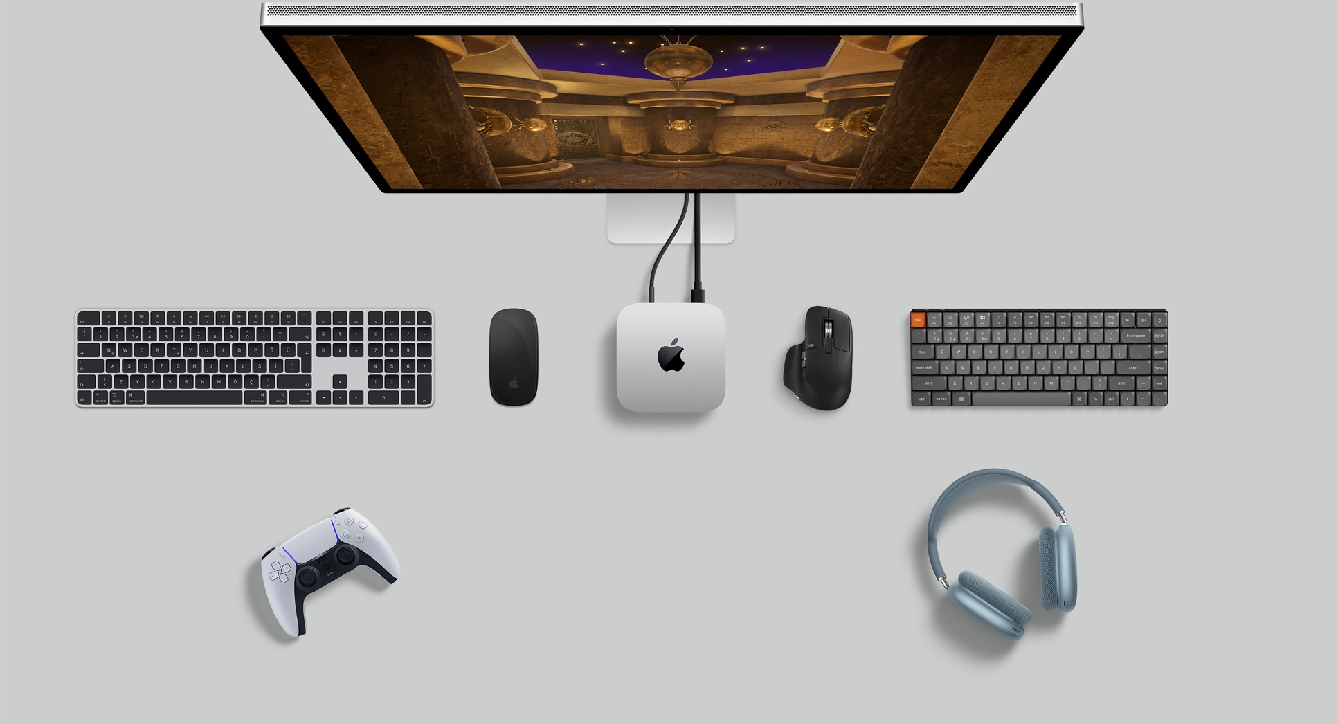 Gümü? rengi Mac mini, bir ekran, kablosuz klavyeler, kablosuz mouse’lar, bir oyun kumandas? ve AirPods Max’in bulundu?u masa düzeninin üstten g?rünümü