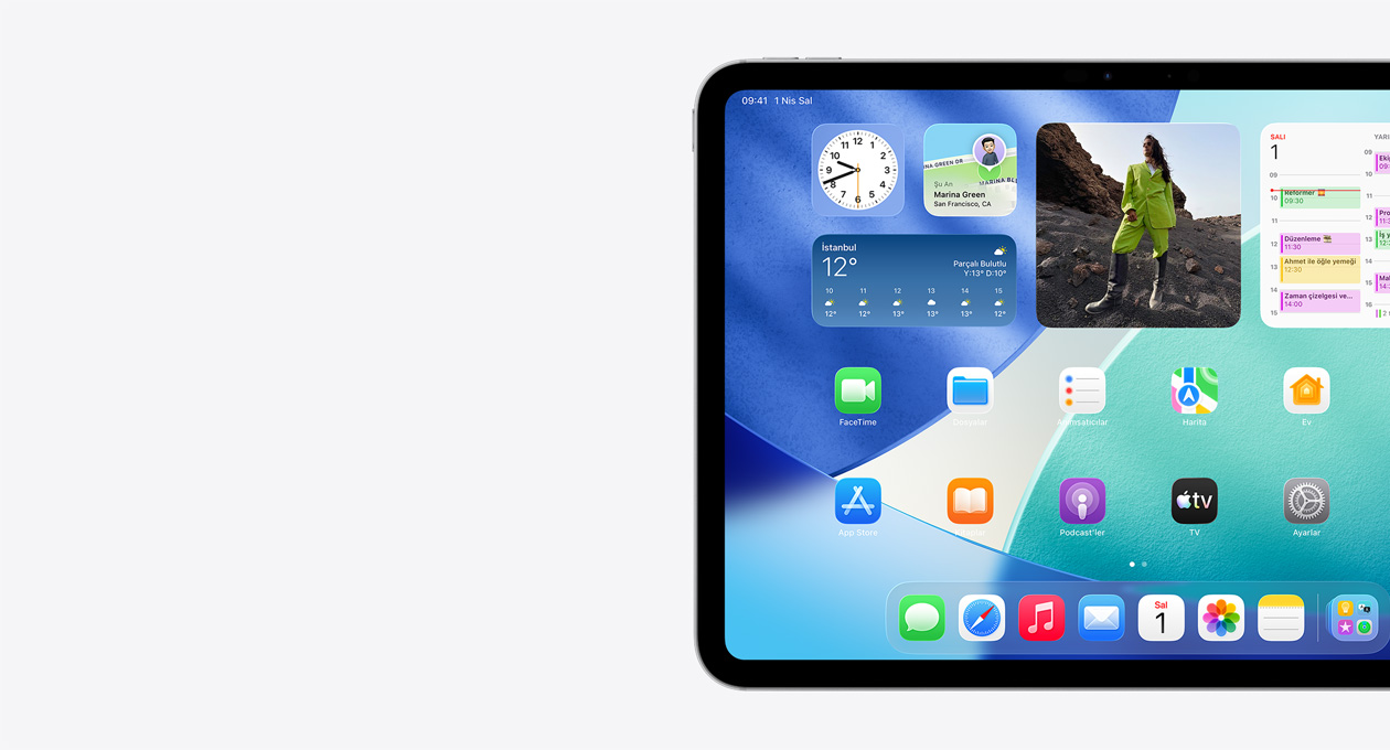 iPad, yatay pozisyonda, ekran?n yaln?zca sol taraf? g?rülüyor, Ana Ekran’da Liquid Glass efekti g?steren yar? saydam saat, Bul uygulamas? ve Hava Durumu ara? tak?m?lar?, iki s?ra halinde daha kü?ük uygulamalar ve Dock yer al?yor