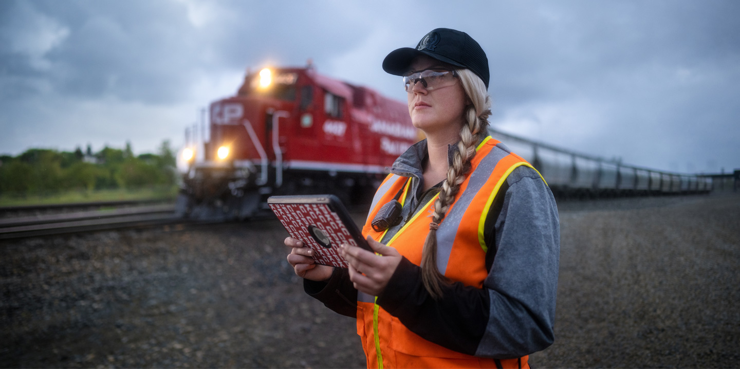 Eine Bahnmitarbeiterin h?lt ein iPad in der Hand und schaut auf die Gleise, w?hrend ein Zug vorbeif?hrt