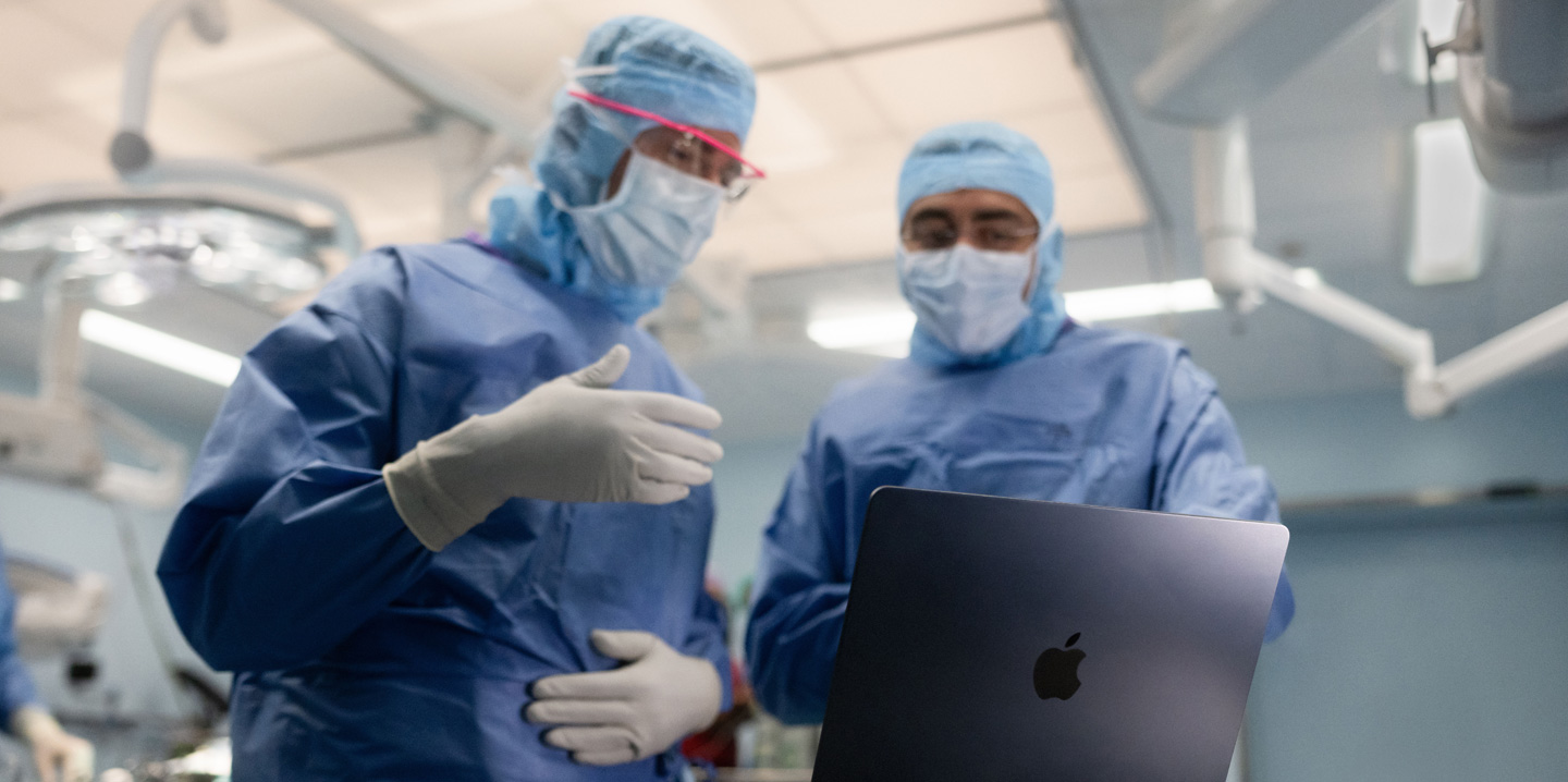 Hai bác s? ph?u thu?t trong phòng m? nhìn vào MacBook, m?t ng??i ra hi?u b?ng tay trong khi ng??i kia quan sát