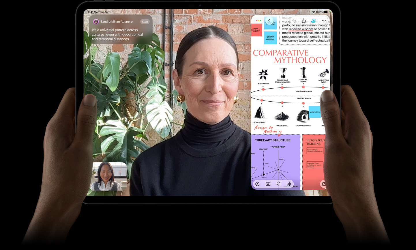 Vista frontal do iPad Pro, preto sideral, m?os a segurar os lados esquerdo e direito do dispositivo na horizontal, ecr? com moldura preta e cantos arredondados, o ecr? apresenta uma conversa no FaceTime com tradu??o em tempo real e uma app educativa com uma apresenta??o intitulada "Mitologia Comparativa" com texto, diagramas e notas escritas à m?o