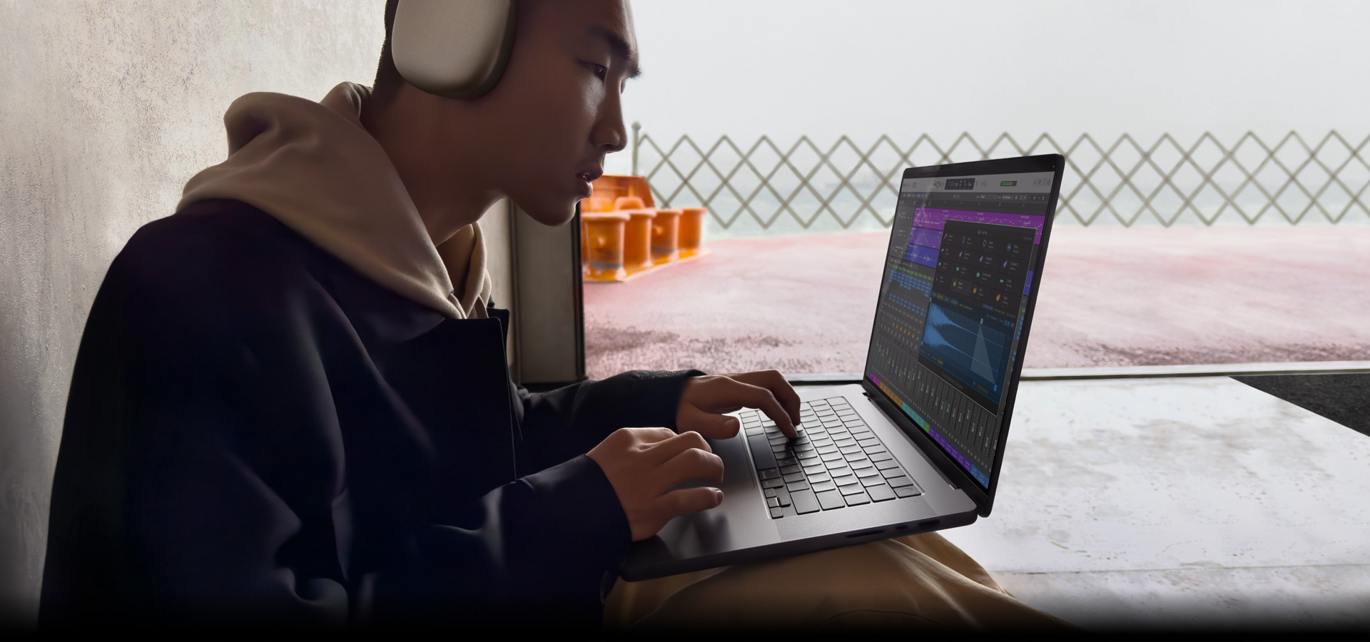 Vista lateral de una persona con unos AirPods Max que está usando Logic Pro en un MacBook Pro de 16 pulgadas, la pantalla muestra el espacio de trabajo de Logic Pro