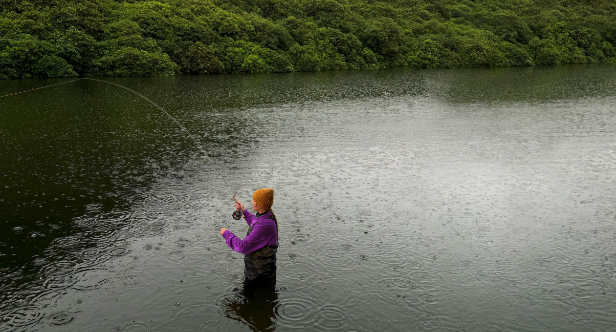Foto de una mujer pescando con mosca en un río, herramienta de Pixelmator Pro que borra un objeto no deseado en el fondo, resaltado en amarillo