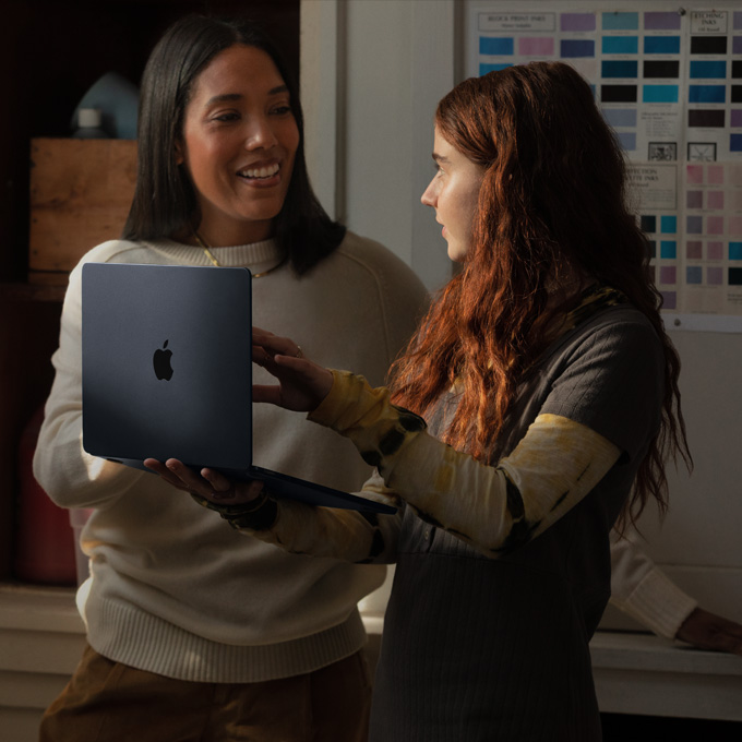 Uma professora e uma aluna conversam enquanto seguram um notebook MacBook
